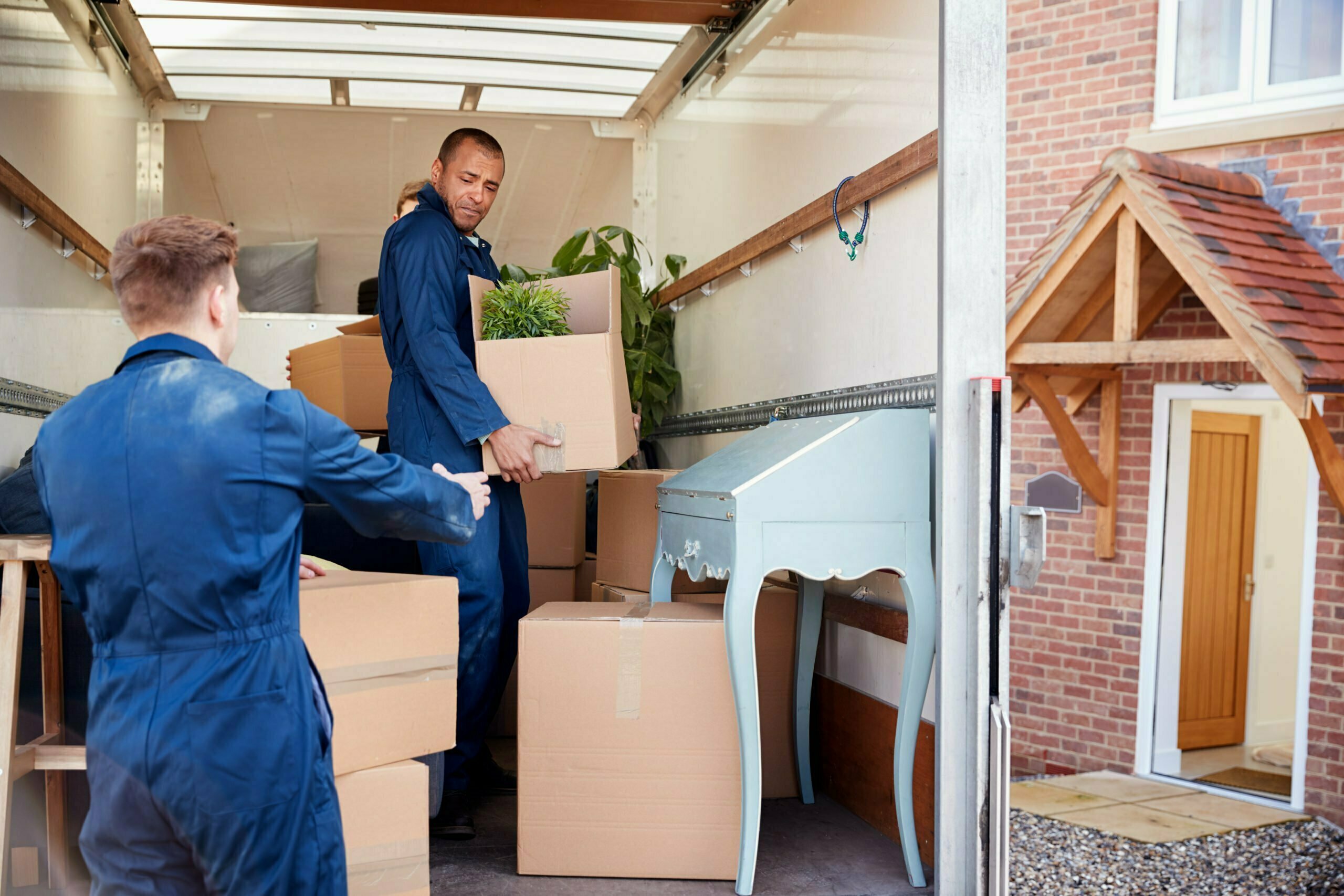 Removal Company Workers Unloading Furniture And Boxes From Truck