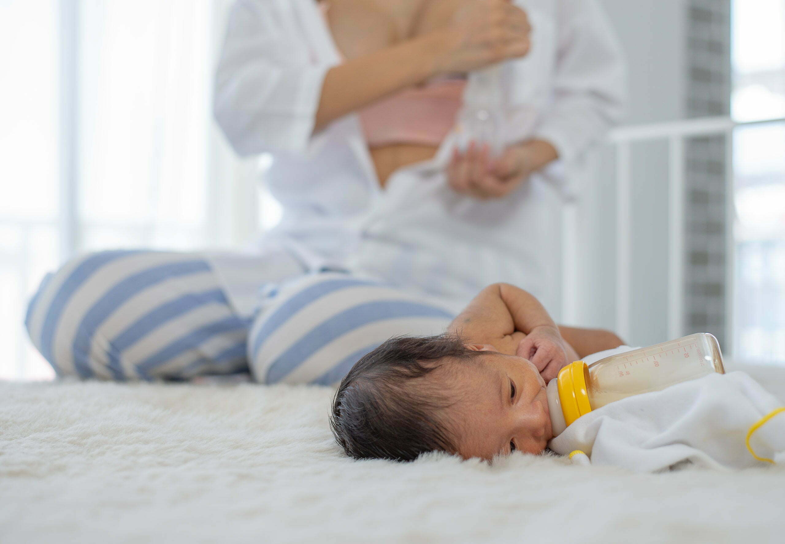 White shirt mother use breast milk pump to get breast milk and sitting near the sleeping newborn