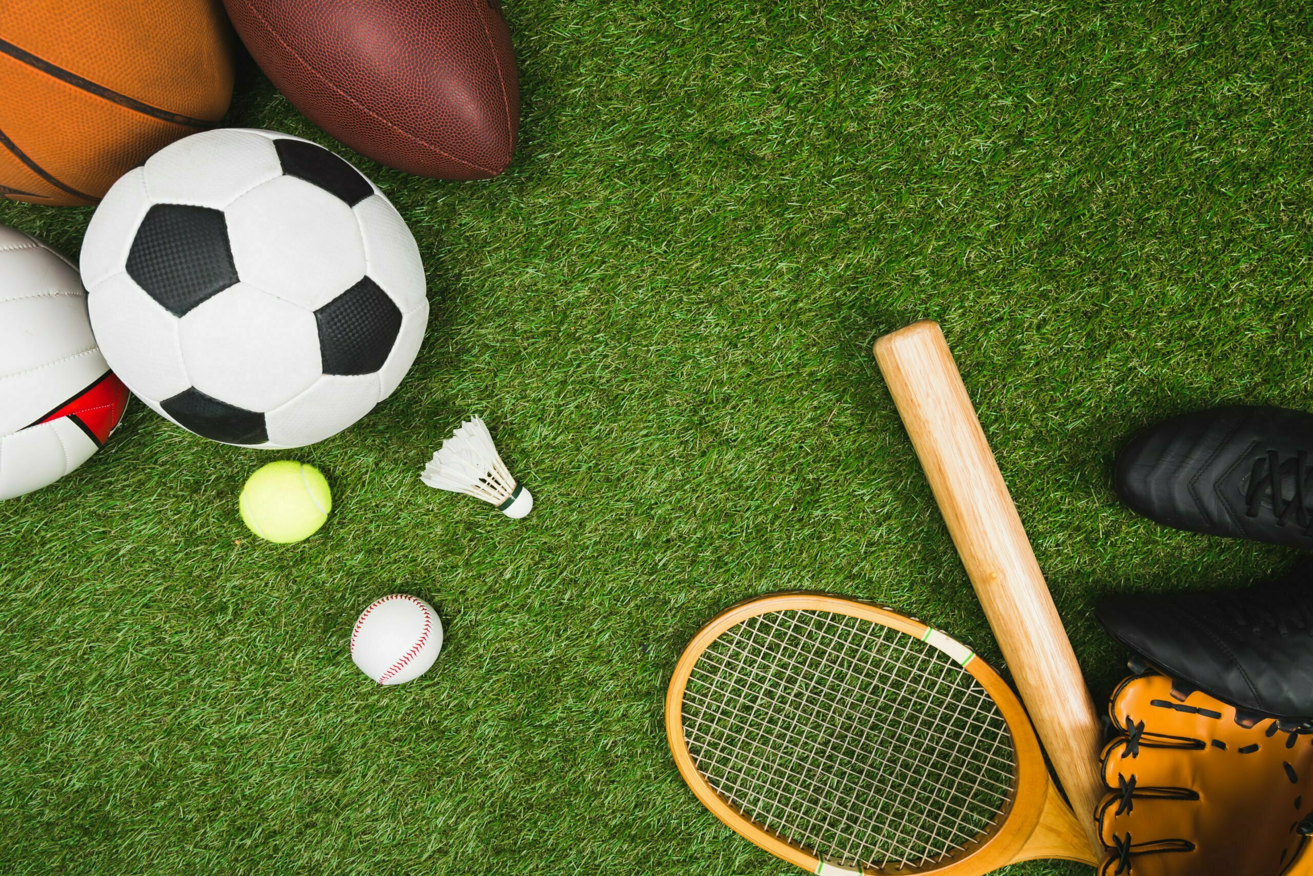 top view of various sport balls, baseball bat and glove, badminton racket on green lawn